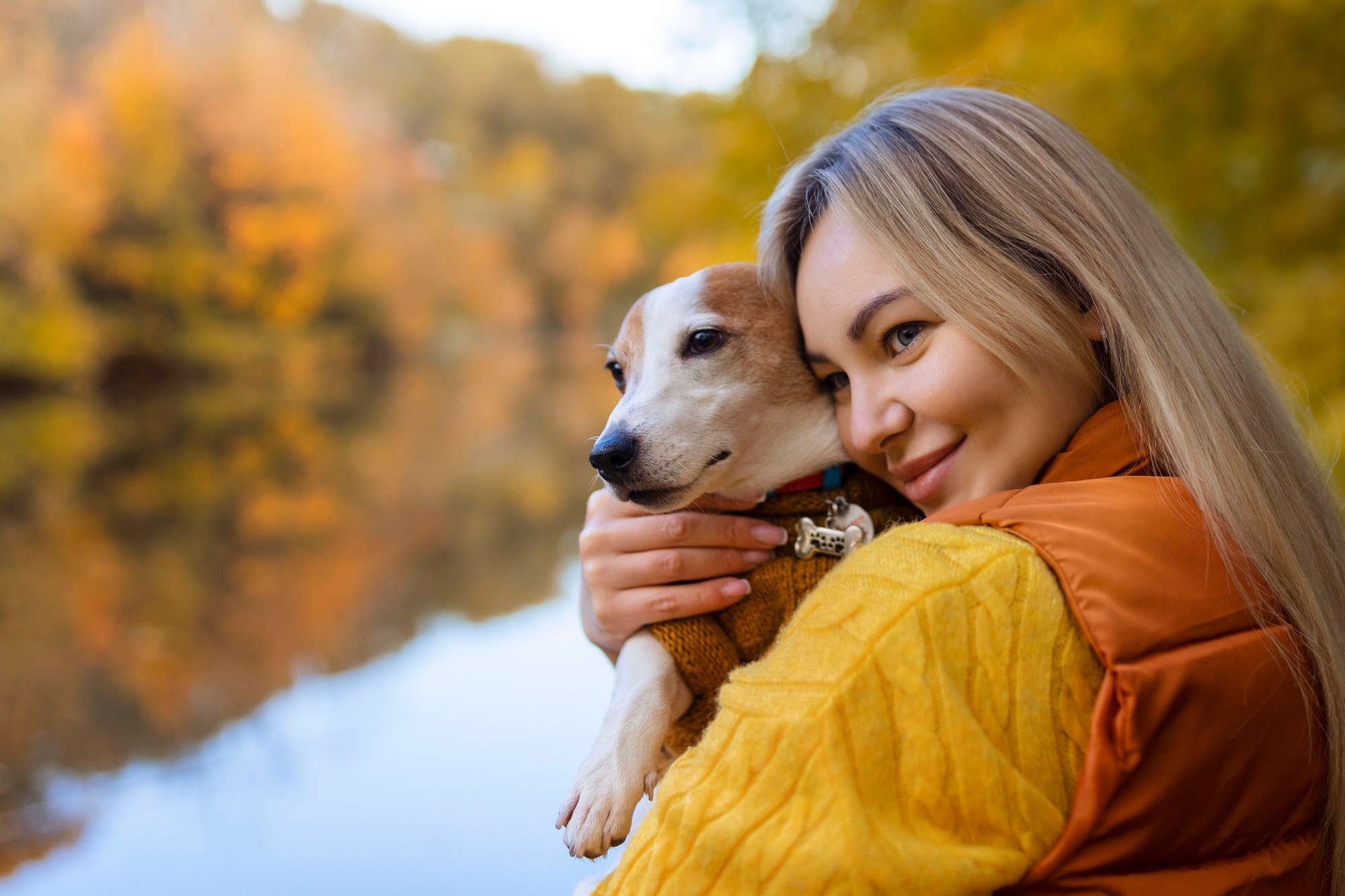 Portrait of a smiling young woman kissing a dog in a field. Dog lover stylish girl hugging her dog